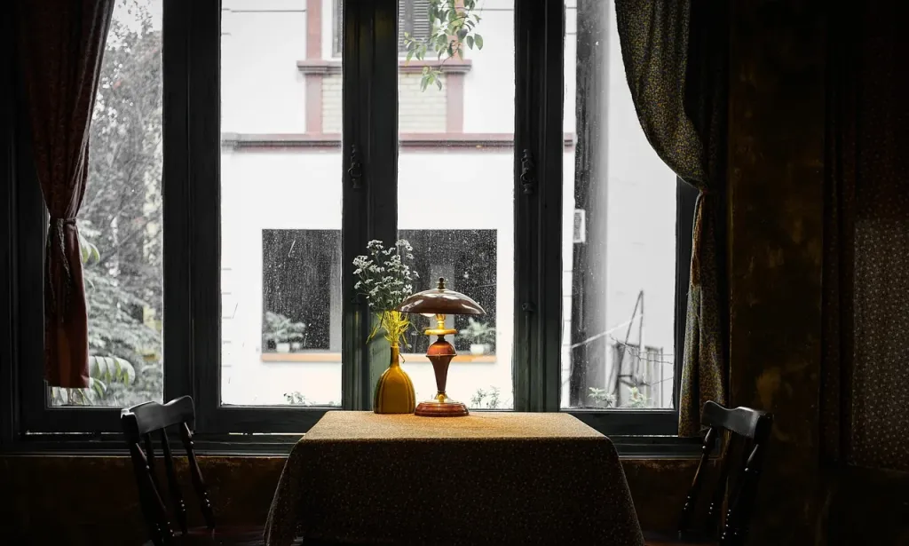 Przytulne wnętrze restauracji z oknem wpadającym do ciemnej sali, tworzące nastrojowy klimat lokalu.